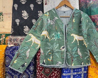 May include: A green quilted jacket with a white trim and a floral and animal print. The jacket is hanging on a hanger and is surrounded by colourful fabrics.