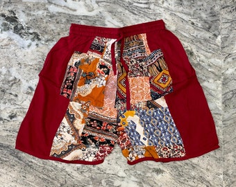 May include: Red patchwork shorts with a floral and geometric print. The shorts have a drawstring waist and are made of a lightweight fabric.