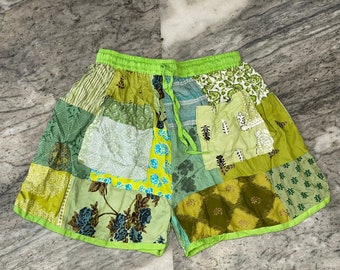 May include: Green patchwork shorts with a lime green elastic waistband and drawstring. The shorts are made of different fabrics with floral and geometric patterns.