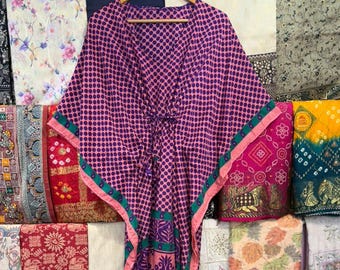 May include: A floor-length kaftan featuring a purple and pink polka dot pattern on the bodice and a purple and pink paisley print on the lower section. The garment has a V-neckline, a drawstring waist, and a teal and pink border trim.