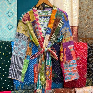 May include: A long-sleeved robe made from a patchwork of various colorful fabrics featuring diverse patterns including geometric shapes, floral motifs, and stripes. The garment includes a matching fabric tie belt at the waist and a shawl collar.