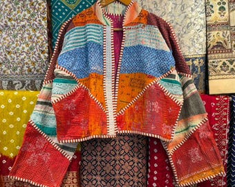 May include: A cropped jacket made from quilted, multi-colored fabric featuring a patchwork of red, orange, blue, and white patterns. The garment has long, wide sleeves, an open front, and visible white stitching along the edges and seams.