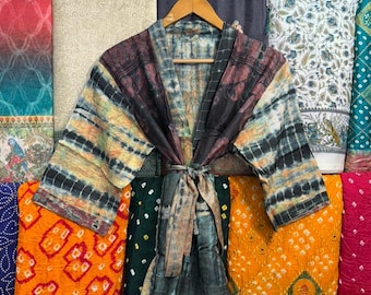 May include: A tie-dye patterned kimono robe with a matching belt, hanging on a wooden hanger. The robe features a mix of colors including black, brown, yellow, and blue. The background showcases various fabric patterns.