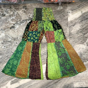 Op de afbeelding: Patchwork palazzo broek in tinten groen, bruin en oranje. De broek heeft een brede, uitlopende pijp en een geplooide tailleband. Verschillende stofpatronen zijn onder meer bloemen- en geometrische ontwerpen.