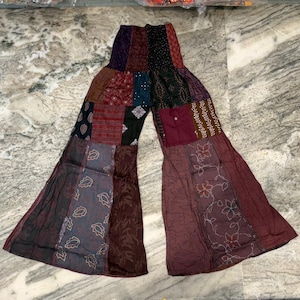 Op de afbeelding: Patchwork palazzo broek in de kleuren bordeaux, marine en bruin. De broek heeft een wijde pijp en is gemaakt van een mix van bedrukte en effen stoffen. Er zit een zak in de taille.