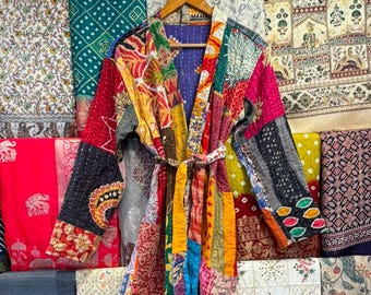 May include: A long-sleeved robe featuring a patchwork design made from various colourful fabrics with intricate patterns. The garment includes a matching tie belt at the waist, a shawl collar, and visible kantha-style stitching throughout the fabric.