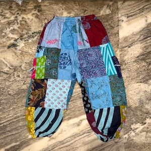 May include: Patchwork pants featuring a variety of colorful fabric squares with diverse patterns including floral, striped, and paisley designs in shades of blue, red, green, and yellow. The trousers have an elastic waistband and gathered cuffs.