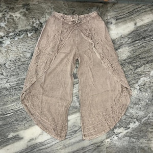 Könnte beinhalten: Hellbraune Palazzo-Hose mit Stickereien an den Kanten. Die Hose hat einen Kordelzug in der Taille und ein weites Bein. Der Stoff scheint leicht und für warmes Wetter geeignet zu sein. Ca. 100 cm lang.