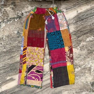 May include: Patchwork pants with a drawstring waist. The pants feature a variety of colorful fabric patches in shades of red, purple, yellow, and blue. The patchwork design creates a unique and bohemian look.