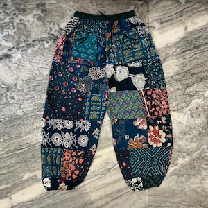 Puede incluir: Pantalones de patchwork con una variedad de patrones florales y geométricos en tonos azules, turquesas, rosas y blancos. Los pantalones tienen cintura con cordón y un ajuste relajado.