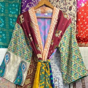 Könnte beinhalten: Eine bunte Seiden-Kimono-Robe mit Patchwork-Muster. Die Robe hat eine lange, fließende Silhouette und wird mit einem Gürtel gebunden. Der Stoff ist eine Mischung aus verschiedenen Mustern und Farben, darunter Grün, Rot, Gelb und Blau.