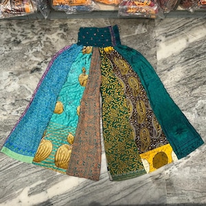 May include: A patchwork wide-leg palazzo pant featuring panels of teal, turquoise, and green fabrics. The panels have various patterns, including paisley, floral, and fruit designs. The waistband is a dark teal color.