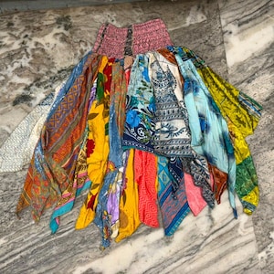 May include: A multi-colored patchwork skirt featuring a smocked elastic waistband. The garment is constructed from various fabric panels in shades of yellow, blue, red, green, and white, displaying diverse floral, geometric, and paisley patterns.