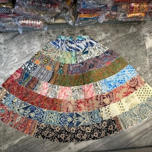 Puede incluir: Una falda patchwork multicolor con varios paneles de tela. La falda presenta estampados florales, paisley y geométricos en tonos azules, rojos, verdes y crema. La falda está sobre una superficie de mármol gris.