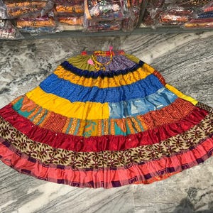 Könnte beinhalten: Ein farbenfroher, mehrschichtiger Rock mit Patchwork-Design. Der Rock weist eine Vielzahl von leuchtenden Farben auf, darunter Gelb, Blau, Rot und Rosa. Der Rock hat einen Kordelzug in der Taille und ist aus leichtem Stoff gefertigt.