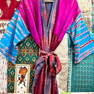 May include: A long, pink, blue, and gray silk robe with a tie belt. The robe has a tie-dye pattern and is made of a soft, flowing fabric.