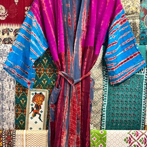 May include: A long, colorful tie-dye robe with a blue and red striped pattern. The robe has a sash tie and a pocket on the left side.