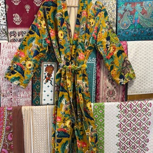 May include: A yellow floral patterned robe with a long sleeve and a tie belt. The robe is made of a soft, velvet-like fabric.