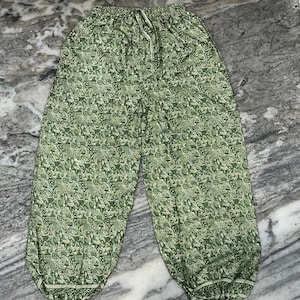 May include: Green patterned trousers with a drawstring waist. The trousers feature a repeating floral design in shades of green and white. The trousers have a relaxed fit and are made of a lightweight fabric.