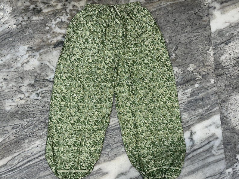 May include: Green patterned trousers with a drawstring waist. The trousers feature a repeating floral design in shades of green and white. The trousers have a relaxed fit and are made of a lightweight fabric.