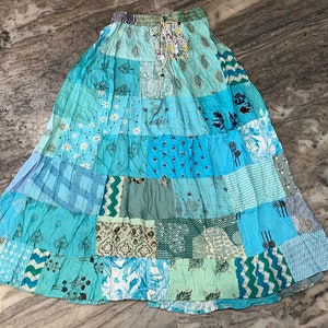 Puede incluir: Una falda larga de patchwork azul con una variedad de patrones florales y geométricos. La falda tiene una cintura con cordón y está hecha de algodón.