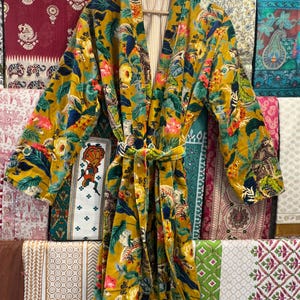 May include: A yellow, green, and pink floral print robe with a long sleeve and a tie belt. The robe is made of a soft, velvety fabric.