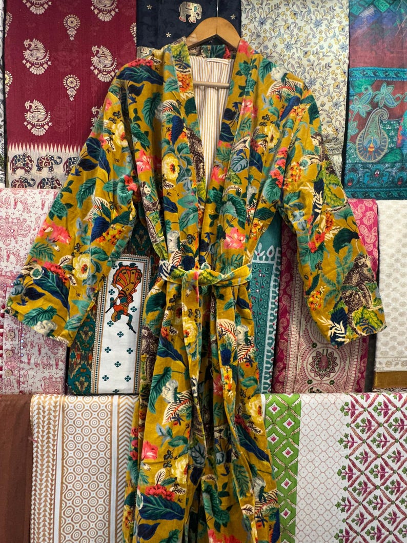 May include: A yellow, green, and pink floral print robe with a long sleeve and a tie belt. The robe is made of a soft, velvety fabric.