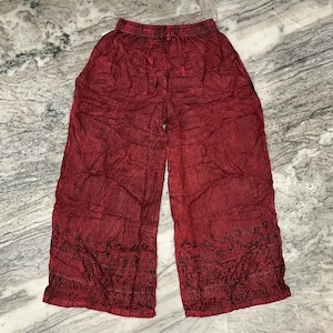 May include: Red wide-leg pants with an elastic waistband and drawstring. The pants have a textured appearance and embroidered detailing along the bottom hem. The fabric appears to be lightweight and suitable for warm weather.