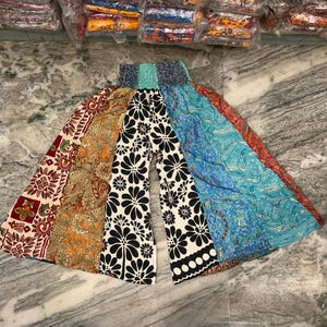 Könnte beinhalten: Bunte Patchwork-Hose mit weitem Bein. Die Hose hat verschiedene Muster, darunter Blumen-, Paisley- und geometrische Drucke in Rot-, Orange-, Schwarz-, Weiß- und Blautönen. Der Bund ist farbenfroh.