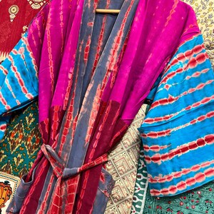 May include: A colorful tie-dye silk robe with a pink, blue, and red pattern. The robe has a sash tie and long sleeves.
