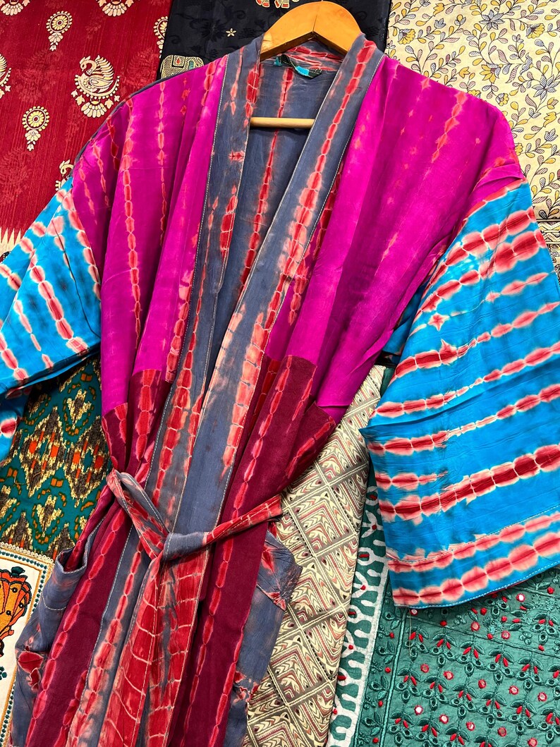 May include: A colorful tie-dye silk robe with a pink, blue, and red pattern. The robe has a sash tie and long sleeves.