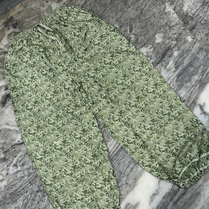 May include: Green patterned trousers with a drawstring waist. The trousers feature a repeating floral design in shades of green and white. The fabric appears lightweight and suitable for casual wear.