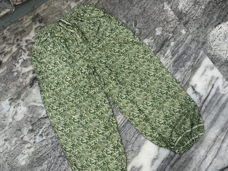 May include: Green patterned trousers with a drawstring waist. The trousers feature a repeating floral design in shades of green and white. The fabric appears lightweight and suitable for casual wear.