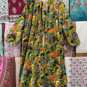May include: A long, yellow, floral patterned robe with a tie belt. The robe has a green, blue, and red floral pattern with a variety of birds and animals.