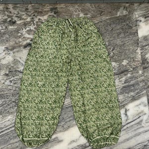 May include: Green patterned trousers with an elasticated waistband and drawstring. The trousers feature a repeating floral design in shades of green and white. The trousers have a relaxed fit and are made of a lightweight fabric.