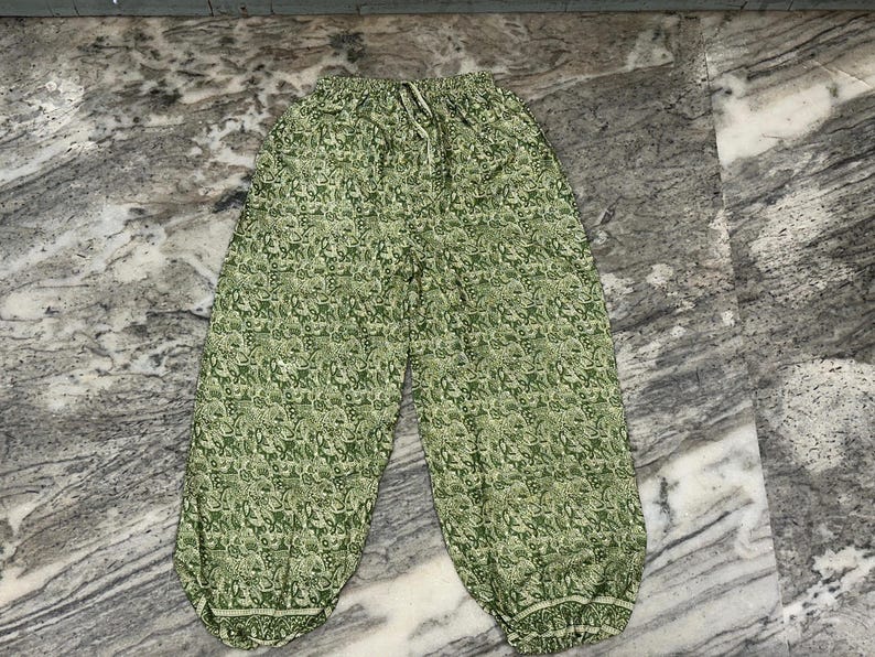 May include: Green patterned trousers with an elasticated waistband and drawstring. The trousers feature a repeating floral design in shades of green and white. The trousers have a relaxed fit and are made of a lightweight fabric.
