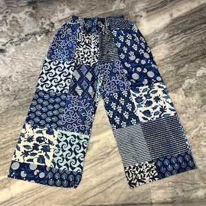 May include: Blue and white patterned palazzo trousers with a patchwork design. The trousers have an elastic waistband and a loose, flowing fit.