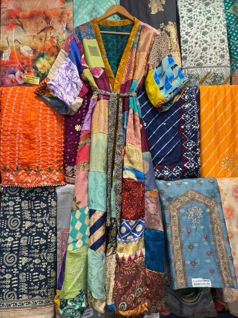 May include: A patchwork kimono robe with a variety of colorful fabric patterns. The robe has a V-neck, long sleeves, and a matching belt. The background features various textiles in shades of orange, blue, and purple.