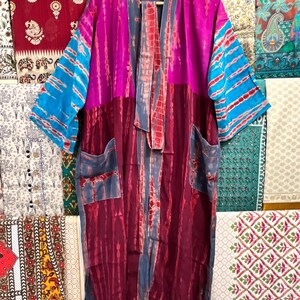 May include: A long, tie-dye kimono with a pink, blue, and red color scheme. The kimono has a tie-dye pattern and is made of a soft, flowing fabric. It has a wide, open collar and long sleeves. The kimono is perfect for layering over a simple outfit or for wearing on its own.