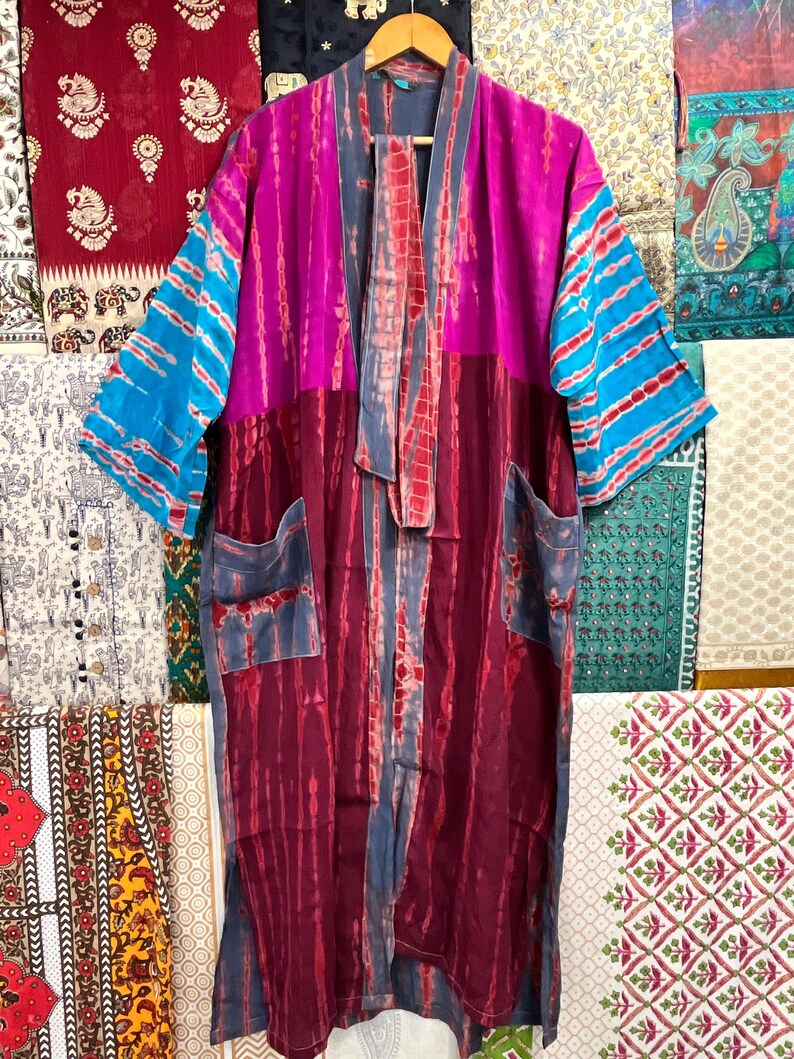 May include: A long, tie-dye kimono with a pink, blue, and red color scheme. The kimono has a tie-dye pattern and is made of a soft, flowing fabric. It has a wide, open collar and long sleeves. The kimono is perfect for layering over a simple outfit or for wearing on its own.