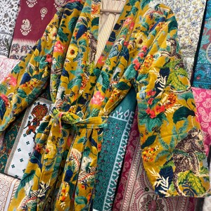 May include: A yellow velvet robe with a floral and animal print. The robe has a tie belt and long sleeves.
