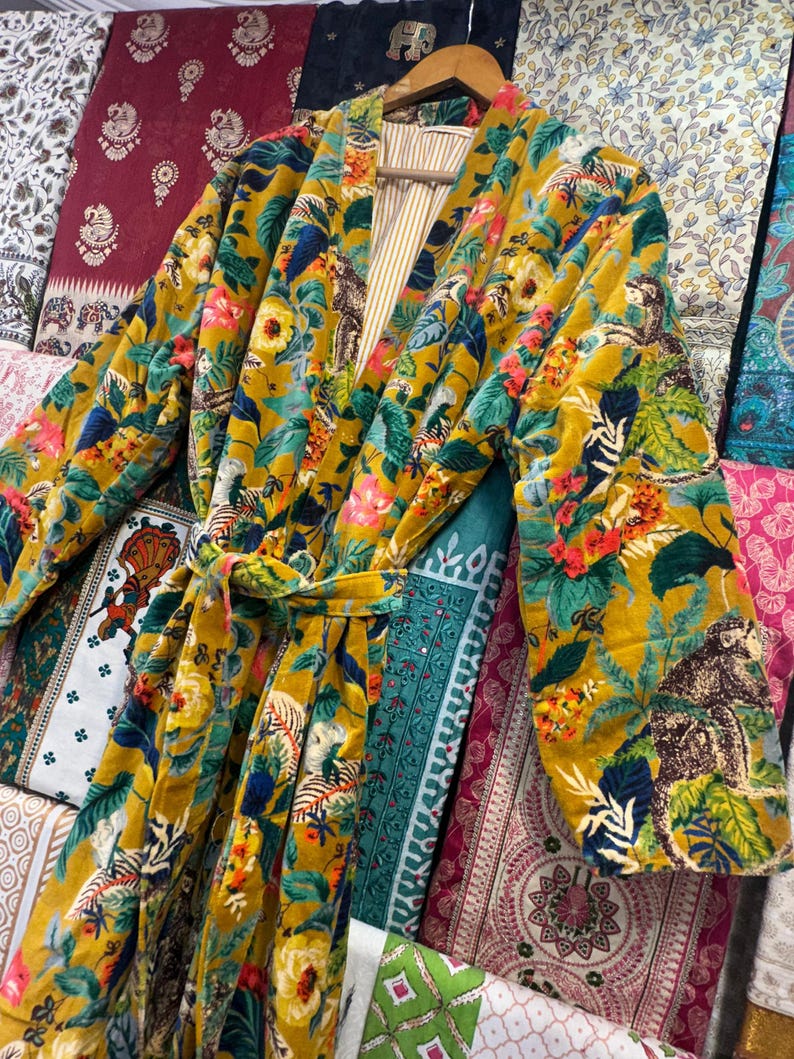 May include: A yellow velvet robe with a floral and animal print. The robe has a tie belt and long sleeves.