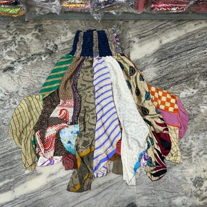 Può includere: Una gonna patchwork con una fascia elastica blu scuro. La gonna presenta una varietà di pannelli di tessuto colorati con motivi tra cui strisce, floreali e geometrici. La gonna è realizzata in materiale leggero.