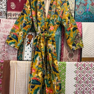 May include: A yellow velvet robe with a floral and animal print. The robe has a tie belt and a striped lining.
