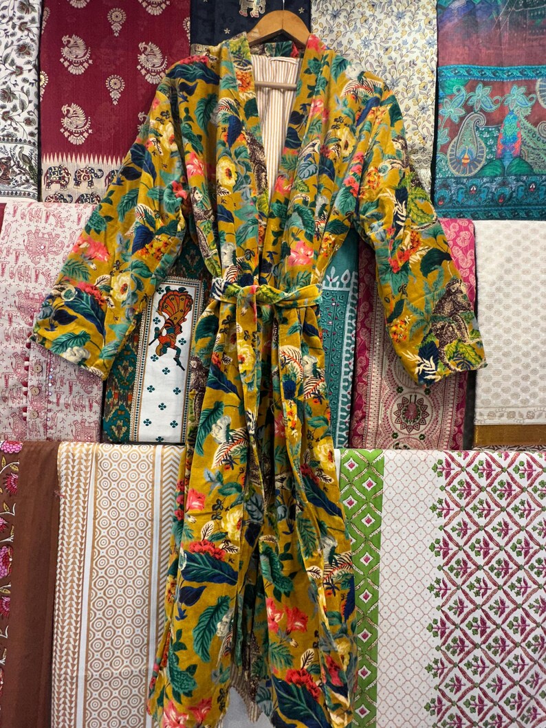 May include: A yellow velvet robe with a floral and animal print. The robe has a tie belt and a striped lining.