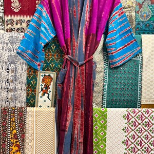 May include: A long, flowing robe with a tie belt. The robe is made of a soft, silky fabric and features a tie-dye pattern in shades of pink, blue, and purple. The robe has long sleeves and a deep V-neck.