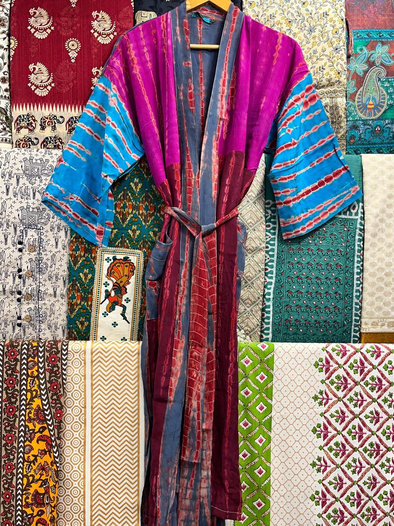 May include: A long, flowing robe with a tie belt. The robe is made of a soft, silky fabric and features a tie-dye pattern in shades of pink, blue, and purple. The robe has long sleeves and a deep V-neck.