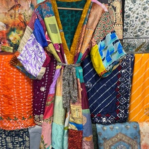May include: A patchwork kimono robe with a variety of colorful fabric patterns. The robe has a gold-colored trim and a matching belt. The background features various textiles in shades of orange, blue, and green.