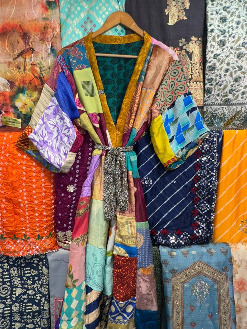 May include: A patchwork kimono robe with a variety of colorful fabric patterns. The robe has a gold-colored trim and a matching belt. The background features various textiles in shades of orange, blue, and green.