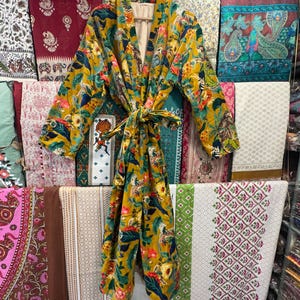 May include: A mustard yellow kimono robe with a floral and animal print. The robe has a tie belt and long sleeves.